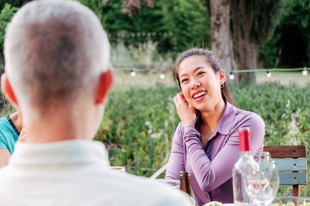 Giovane donna asiatica adulta sorridente e parlando con gli amici in una cena seduta al cortile