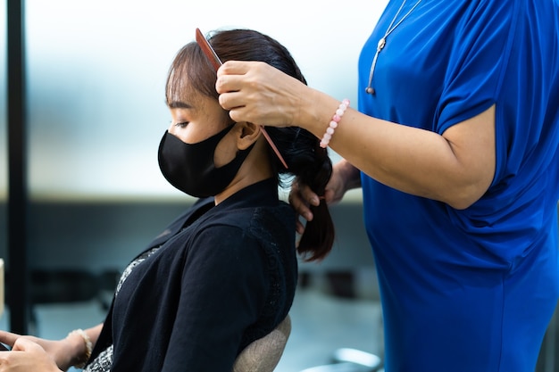 Giovane donna asiatica al parrucchiere che indossa la maschera protettiva chirurgica. Nuovo concetto di allontanamento normale e sociale