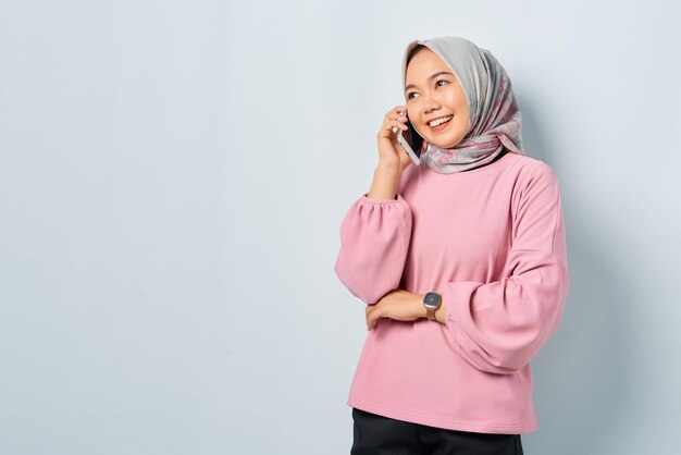 Giovane donna asiatica allegra in camicia rosa che parla sul telefono cellulare isolato sopra priorità bassa bianca