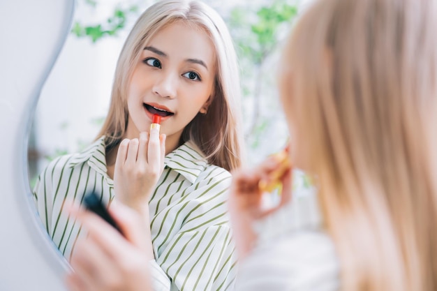 Giovane donna asiatica che applica il rossetto davanti allo specchio