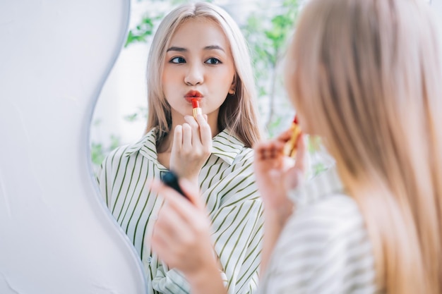 Giovane donna asiatica che applica il rossetto davanti allo specchio