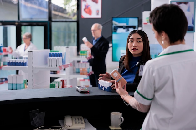 Giovane donna asiatica che chiede al cassiere della farmacia la protezione solare al banco del negozio medico al dettaglio. Acquisto del cliente in farmacia e consulenza con uno specialista farmaceutico alla cassa