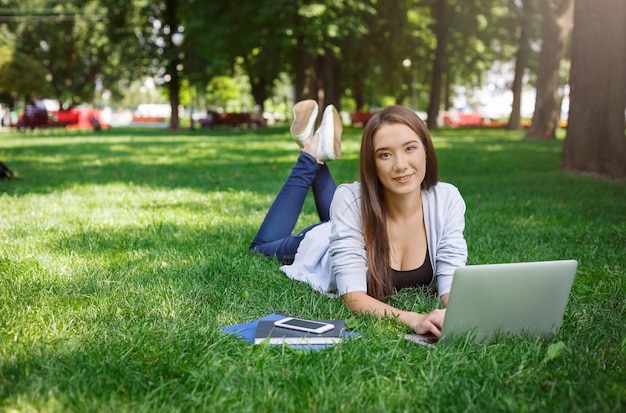 Giovane donna asiatica che digita, posa su un'erba verde. Lavorare con il laptop nel parco vicino a smartphone e libri. Concetto di stile di vita e tecnologia