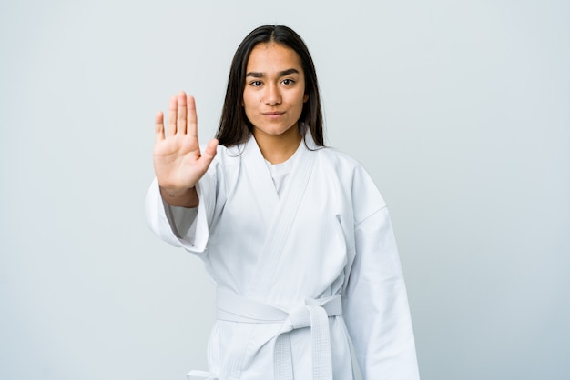 Giovane donna asiatica che fa karate isolato sul muro bianco in piedi con la mano tesa che mostra il segnale di stop, impedendoti.