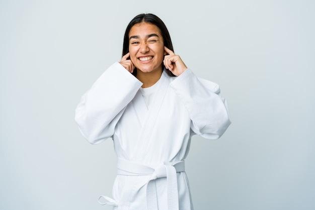 Giovane donna asiatica che fa karate isolato sulle orecchie del rivestimento murale bianco con le mani.