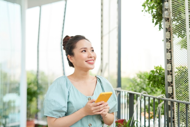 Giovane donna asiatica che gode della natura e utilizza il telefono sul balcone