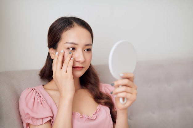 Giovane donna asiatica che guarda allo specchio. Concetto di cura del corpo