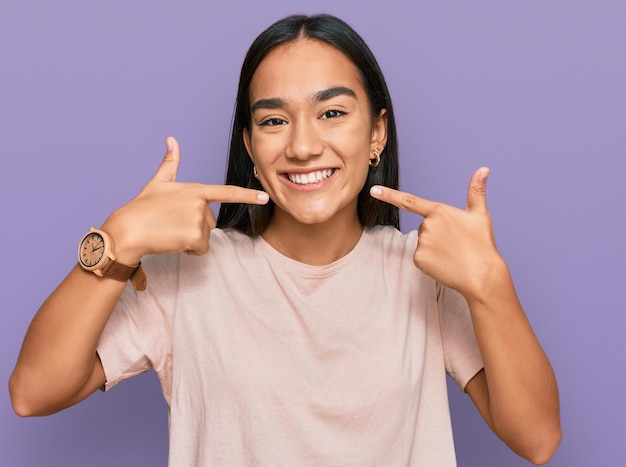 Giovane donna asiatica che indossa abiti casual sorridendo allegro mostrando e indicando con le dita i denti e il concetto di salute dentale della bocca