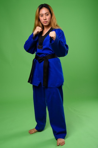 giovane donna asiatica che indossa il karate blu Gi contro lo spazio verde