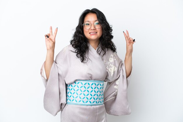 Giovane donna asiatica che indossa il kimono isolato su sfondo bianco che mostra il segno di vittoria con entrambe le mani