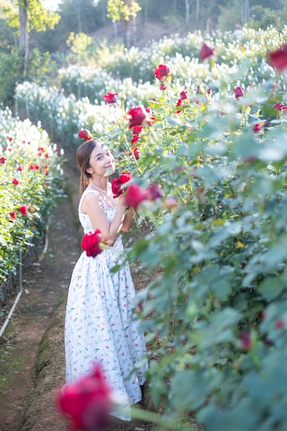 Giovane donna asiatica che indossa un abito bianco posa con una rosa nel roseto