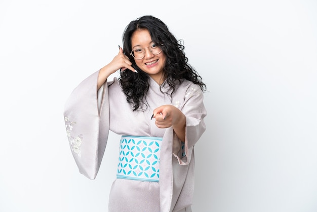 Giovane donna asiatica che indossa un kimono isolato su sfondo bianco che fa il gesto del telefono e indica la parte anteriore