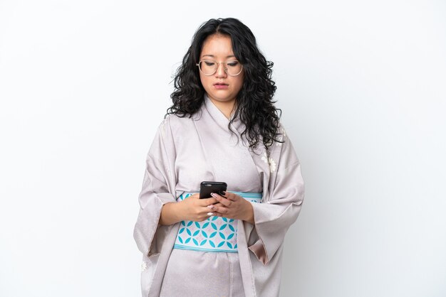 Giovane donna asiatica che indossa un kimono isolato su sfondo bianco inviando un messaggio con il cellulare