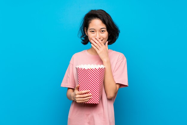 Giovane donna asiatica che mangia i popcorn con espressione facciale di sorpresa