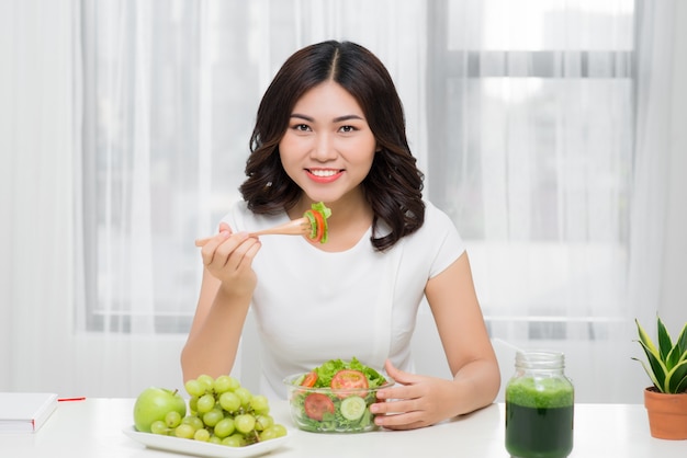 Giovane donna asiatica che mangia insalata fresca a casa