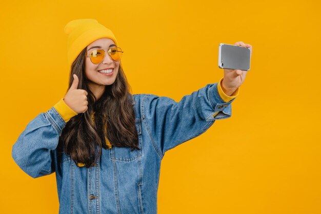 Giovane donna asiatica che mostra il pollice in su e scatta una foto selfie sullo smartphone