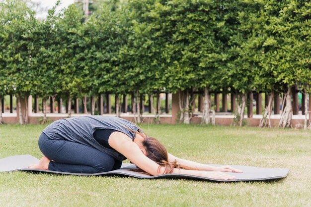 Giovane donna asiatica che pratica yoga all'aperto in posa meditata seduta sull'erba verde con gli occhi chiusi in natura un parco giardino campo, stretching, meditazione, concetto di assistenza sanitaria esercizio