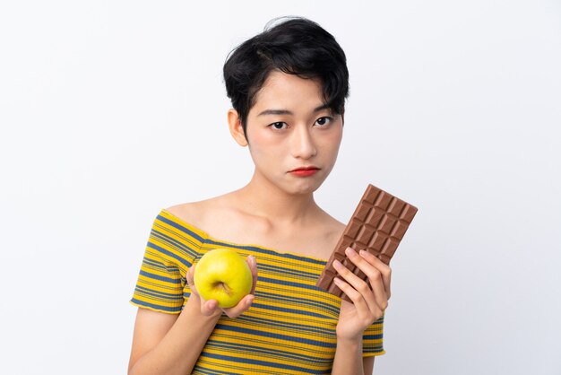 Giovane donna asiatica che prende una compressa di cioccolato in una mano e una mela nell'altra