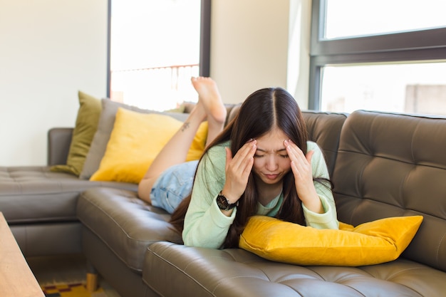 Giovane donna asiatica che sembra stressata e frustrata, lavorando sotto pressione con un mal di testa e turbata da problemi