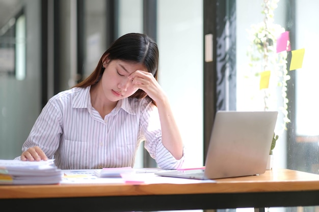 Giovane donna asiatica che sente ceppo di testa di emicrania Stanco Finanziere donna d'affari oberato di lavoro mentre lavora su un computer portatile in ufficio