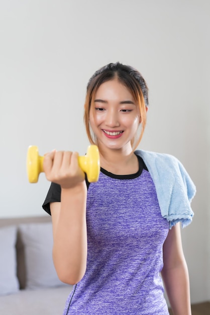 Giovane donna asiatica che si allena e fa esercizio per sollevare manubri per uno stile di vita sano a casa