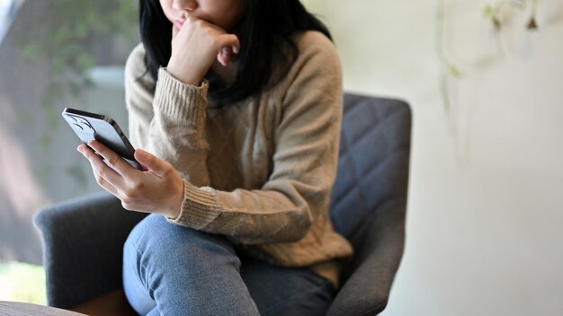 Giovane donna asiatica che si concentra sulla lettura di notizie online sul suo smartphone ritagliata