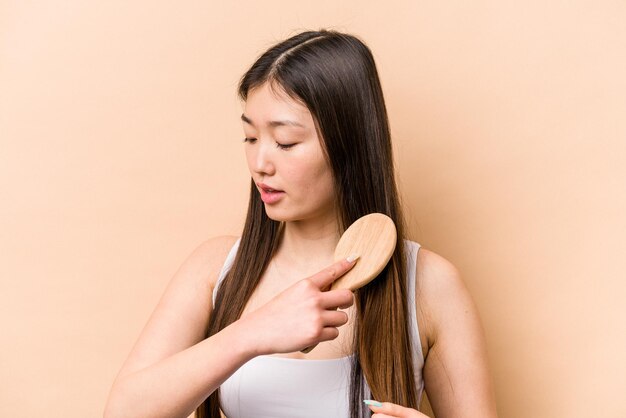 Giovane donna asiatica che si pettina i capelli isolati su sfondo beige