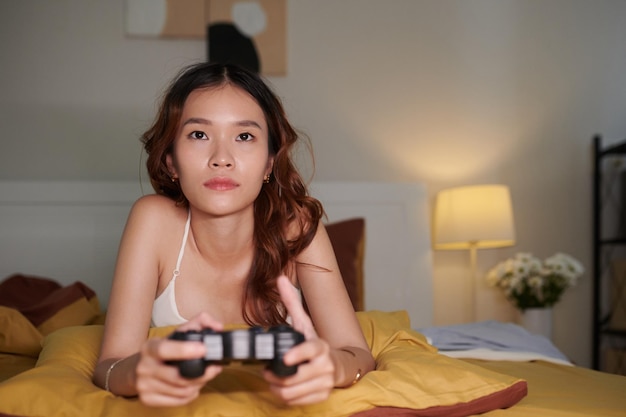 Giovane donna asiatica che si rilassa sul letto e gioca al videogioco