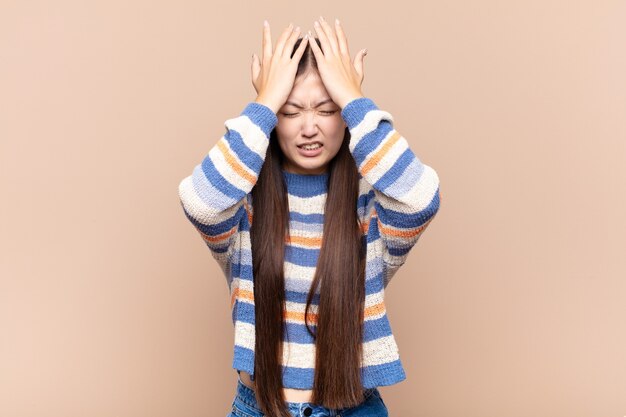 Giovane donna asiatica che si sente stressata e ansiosa, depressa e frustrata con un mal di testa, alzando entrambe le mani alla testa