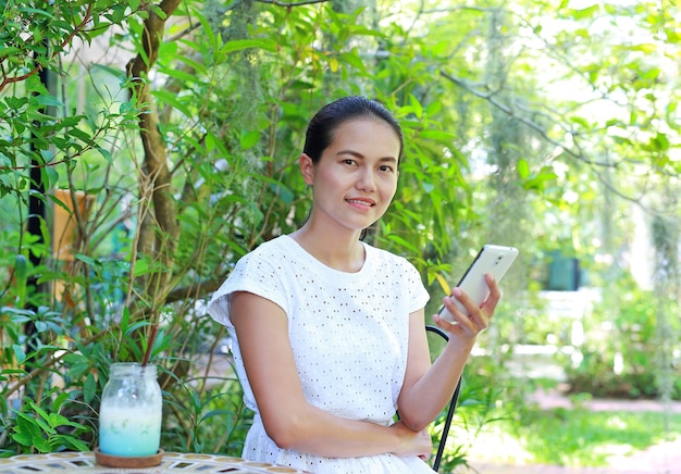 Giovane donna asiatica che si siede al caffè all&#39;aperto e utilizzando smart phone