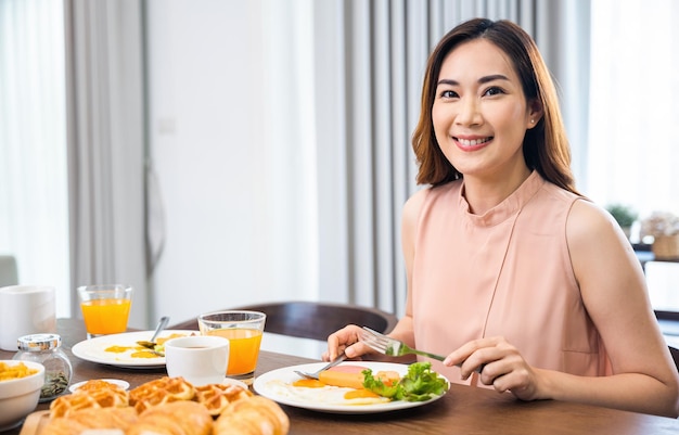 Giovane donna asiatica che si siede al tavolo della cucina mangiando una sana colazione a casa