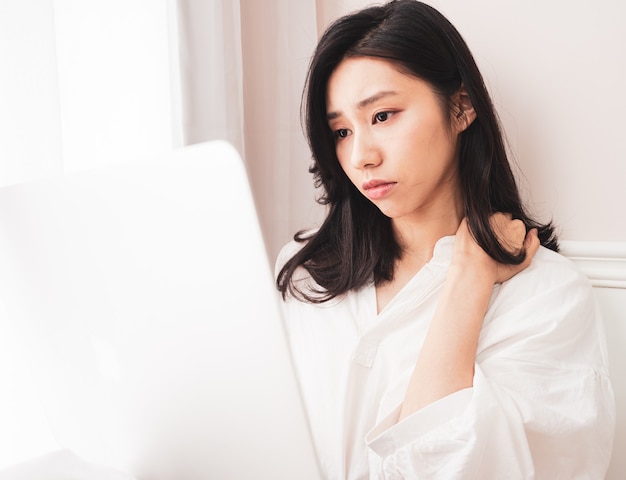 Giovane donna asiatica che soffre di dolore alla spalla quando usa il laptop