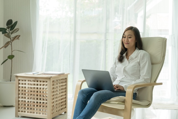 giovane donna asiatica che sorride e si gode il tempo a casa bellissimo lavoro sul laptop a casa