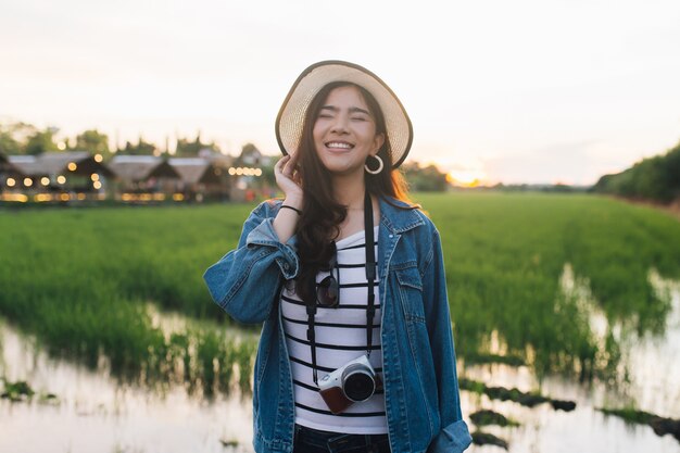 Giovane donna asiatica che sorride in cappello con la macchina fotografica. Ragazza che gode della bellissima natura con sunse