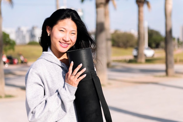Giovane donna asiatica che sorride mentre tiene in mano un tappetino da yoga