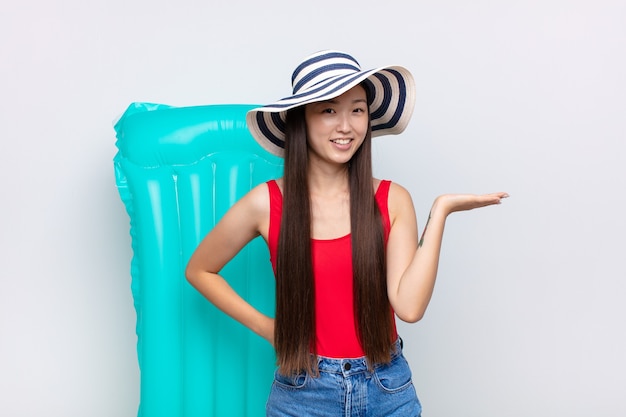 Giovane donna asiatica che sorride, sentendosi sicura, riuscita e felice, mostrando concetto o idea sullo spazio della copia sul lato. concetto di estate