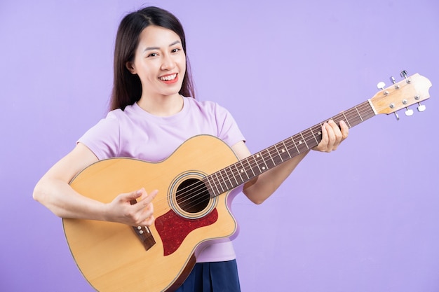 Giovane donna asiatica che suona la chitarra su sfondo viola