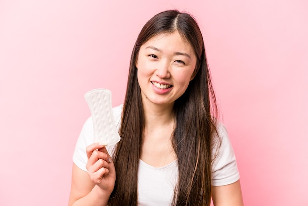 Giovane donna asiatica che tiene assorbente igienico isolato su sfondo rosa ridendo e divertendosi