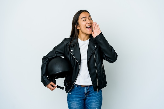 Giovane donna asiatica che tiene un casco della motocicletta sopra la parete isolata che grida e che tiene il palmo vicino alla bocca aperta.