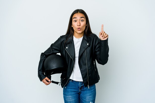 Giovane donna asiatica che tiene un casco della motocicletta sopra la parete isolata che ha qualche grande idea