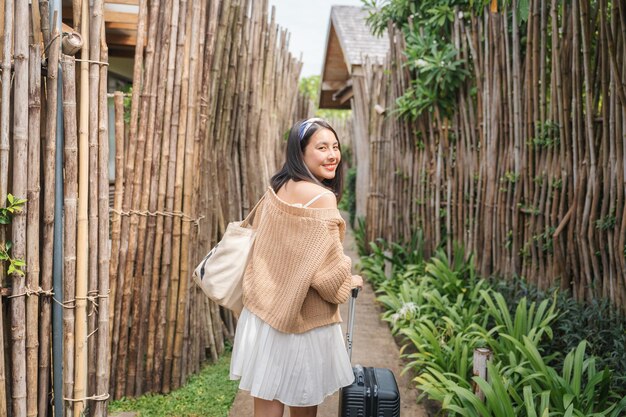 Giovane donna asiatica che trascina un bagaglio nel giardino del resort in vacanza