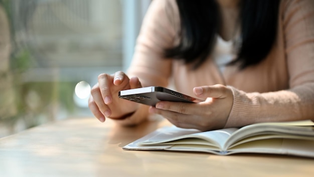 Giovane donna asiatica che usa il suo telefono mentre si rilassa nella biblioteca o nella caffetteria immagine ritagliata