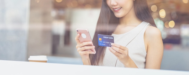 Giovane donna asiatica che usa la carta di credito con il telefono cellulare per lo shopping online nella caffetteria