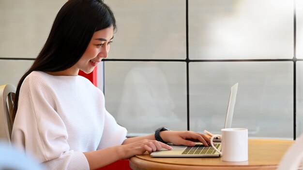 Giovane donna asiatica che utilizza il suo computer portatile in una braciola di caffè.