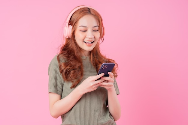 Giovane donna asiatica che utilizza smartphone e ascolta musica su sfondo rosa