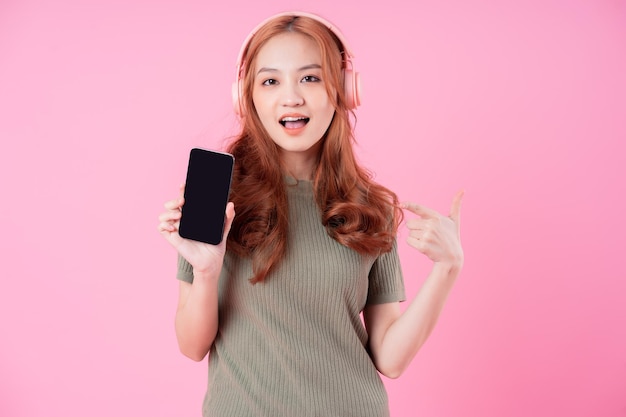 Giovane donna asiatica che utilizza smartphone e ascolta musica su sfondo rosa