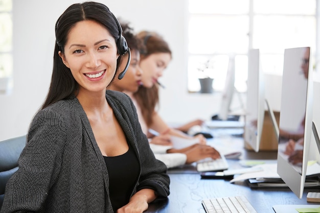 Giovane donna asiatica con auricolare sorridente alla telecamera in ufficio