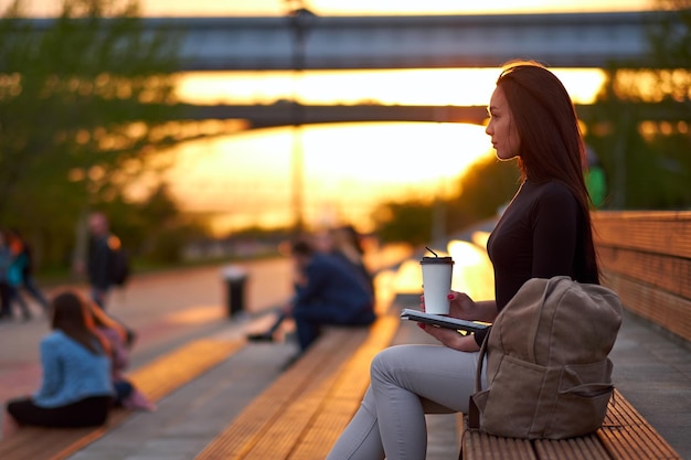 Giovane donna asiatica con caffè e libro la sera al tramonto ritratto della città all'aperto