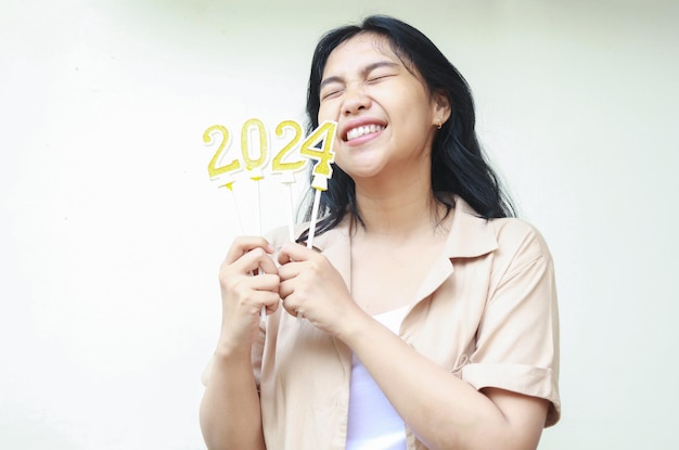 giovane donna asiatica con candele d'oro numeri 2024 e occhio chiuso indossa camicia marrone casual