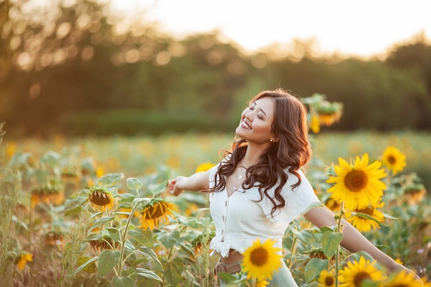 Giovane donna asiatica con capelli ricci in un campo di girasoli al tramonto. Ritratto di una giovane bella donna asiatica al sole. Estate.